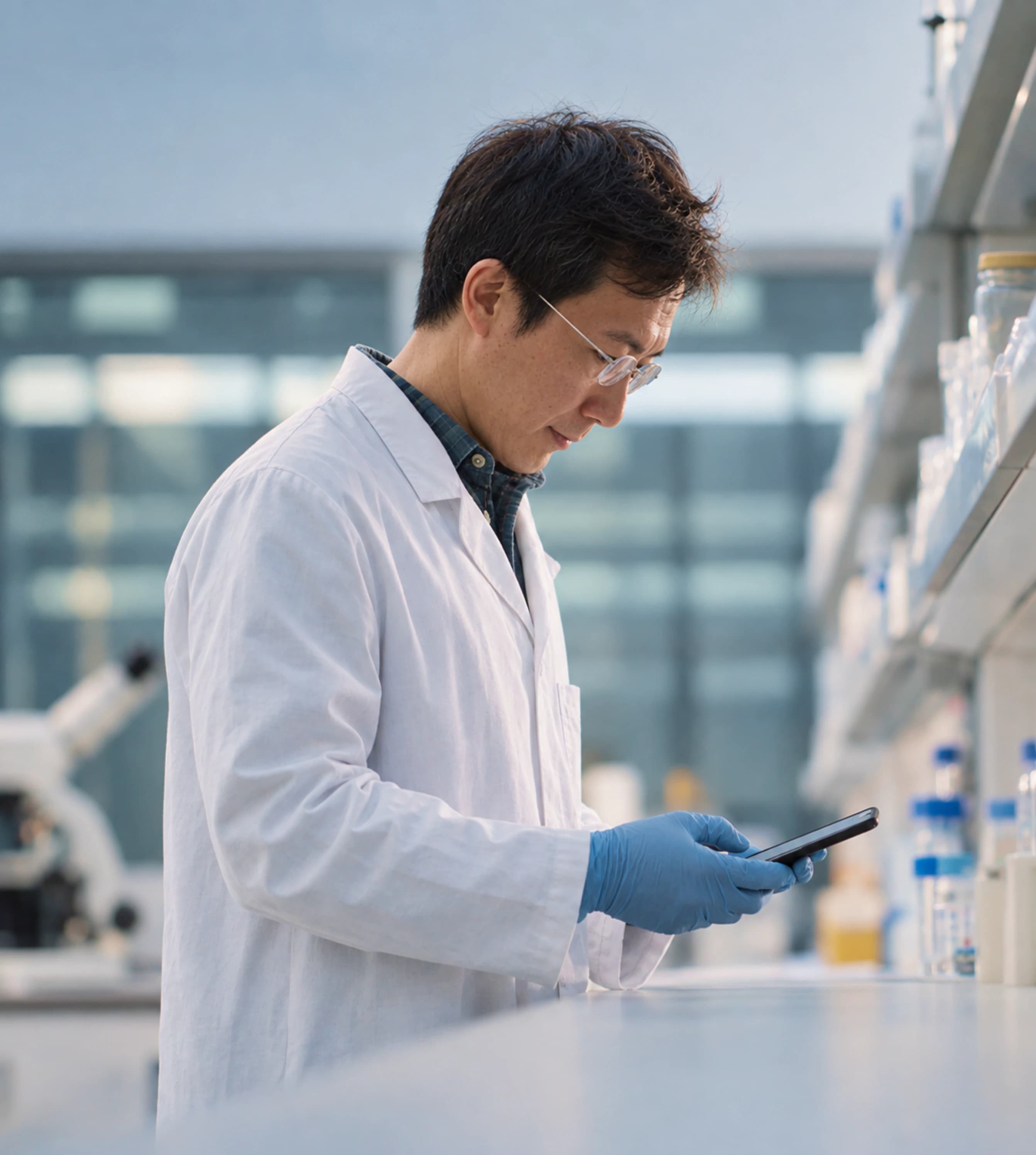 A researcher in a lab coat checking a phone at a laboratory bench
